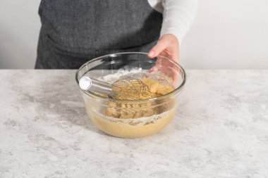 Mixing ingredients with a hand whisk in a large mixing bowl to bake banana cookies with chocolate drizzle.