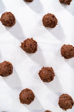 Scooping cookie dough with dough scoop into a baking sheet lined with parchment paper to bake chocolate cookies with chocolate hearts for Valentines Day.