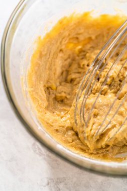 Mixing ingredients with a hand whisk in a large mixing bowl to bake banana cookies with chocolate drizzle.