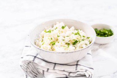 Cilantro Lime Rice. Beyaz seramik kaselerde taze maydanozla süslenmiş kişniş limonlu pirinç servis ediliyor..