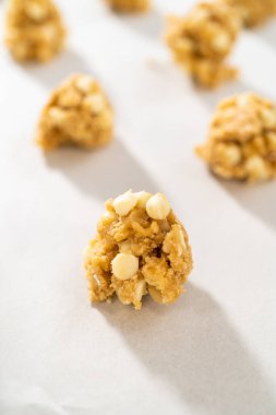 Beyaz çikolatalı macadamia fındığı pişirmek için parşömen kağıdıyla kaplanmış hamur kepçesiyle kurabiye hamuru pişirmek..