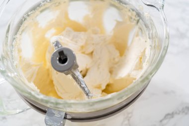 Whisking buttercream frosting in a glass mixing bowl with an electric kitchen mixer for American flag mini cupcakes.