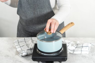 Eriyen beyaz çikolata parçaları ve diğer malzemeler kaynamış suyun üzerine karıştırıp çubuk şekerleme hazırlıyor..