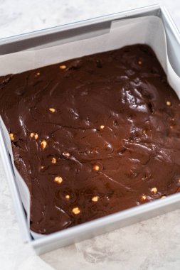 Filling square cheesecake pan lined with parchment paper with fudge mixture to prepare chocolate hazelnut fudge.