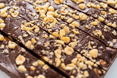 Büyük bir mutfak bıçağıyla çikolatalı fındıklı şekerlemeyi beyaz bir kesme tahtasında kare parçalara ayırmak..