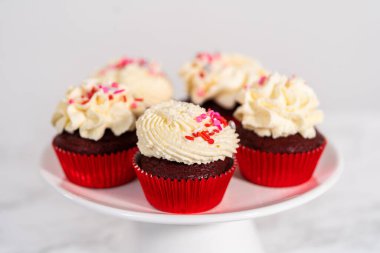 Taze pişmiş kadife kekler, üzerine beyaz çikolata ganache süslemesi serpilmiş..