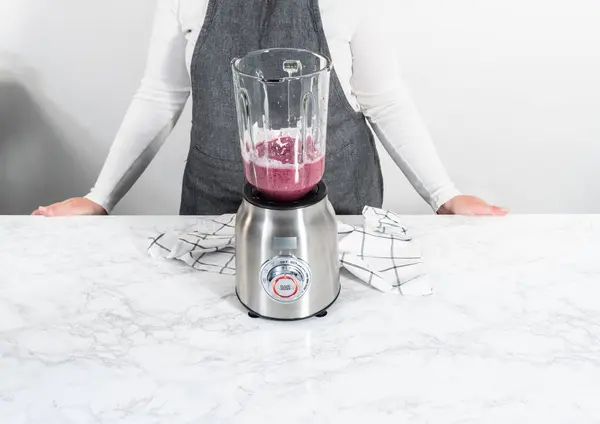 Mixing ingredients in kitchen blender to prepare mixed berry smoothie.