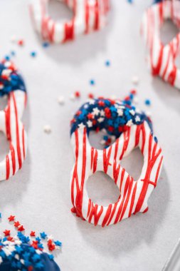 Dipping pretzels twists into melted chocolate to make red, white, and blue chocolate-covered pretzel twists.