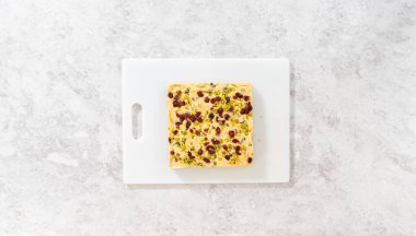 Düz yatıyordu. Böğürtlenli şam fıstıklı şekerlemeyi büyük bir mutfak bıçağıyla beyaz bir kesme tahtasında kare parçalara ayırmak..