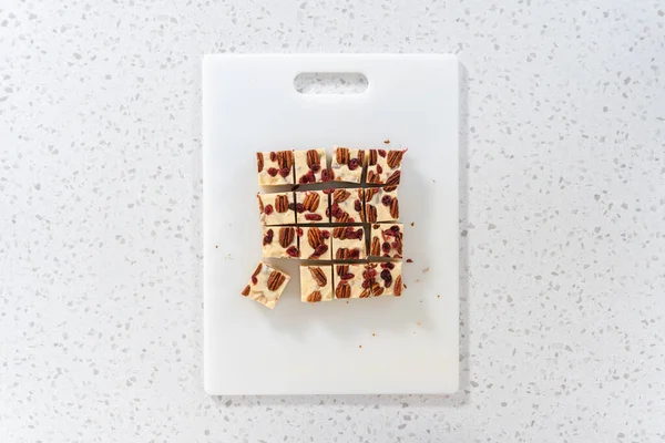 平置きだ 白いチョコレートクランベリーの種を切ることは白いまな板の上の小さな断片になる — ストック写真