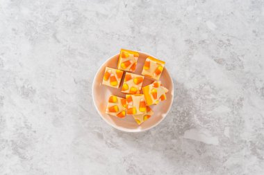 Flat lay. Homemade candy corn fudge square pieces on a white plate.