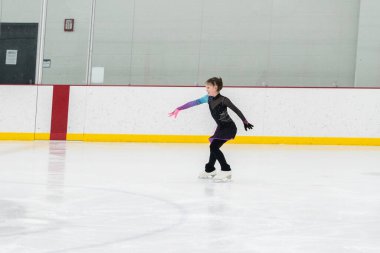 Artistik patinaj rutinini mükemmelleştiren genç bir kız kapalı bir buz pateni sahasında yarışma elbisesini giyerken.