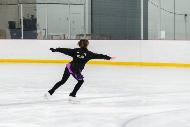 Artistik patinaj rutinini mükemmelleştiren genç bir kız kapalı bir buz pateni sahasında yarışma elbisesini giyerken.