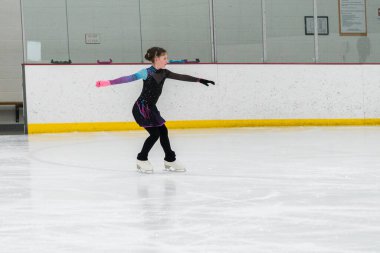 Artistik patinaj rutinini mükemmelleştiren genç bir kız kapalı bir buz pateni sahasında yarışma elbisesini giyerken.