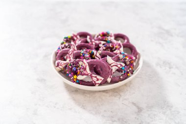 Homemade chocolate-dipped pretzel twists decorated with colorful sprinkles and chocolate mermaid tails on a white plate.