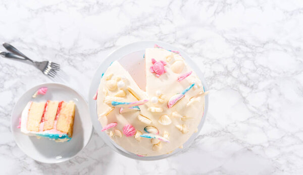 Flat lay. Slicing mermaid-themed 3 layer vanilla cake on a cake stand.