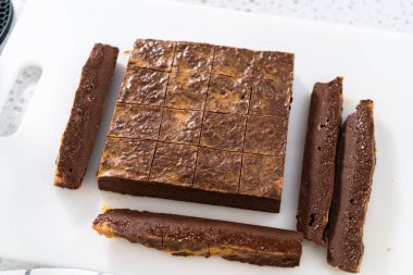 Çikolatalı fıstık ezmeli şekerlemeyi beyaz bir kesme tahtasında küçük parçalara ayırmak..