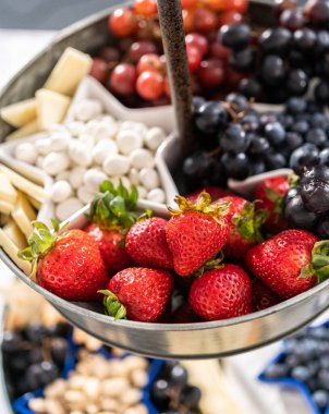 4 Temmuz şarküteri tahtası peynir, kraker, salam ve taze meyve dolu iki katlı bir metal tezgahta.