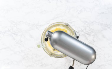 Flat lay. Whisking buttercream frosting in a glass mixing bowl with an electric kitchen mixer for American flag mini cupcakes.