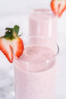 Taze taze çilek ve kağıt kamışla süslenmiş sağlıklı bir kahvaltı muzlu smoothie..