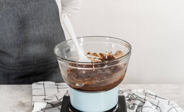 Beyaz çikolata parçacıkları ve diğer malzemeleri kaynayan suyun üzerine karıştırıp çikolatalı macadamia şekerlemesi hazırlıyorum..