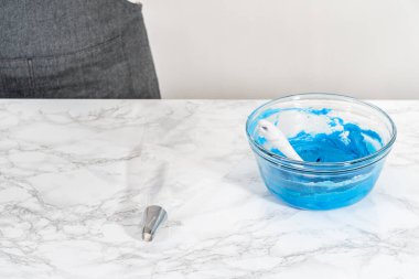 Mixing food coloring into the buttercream frosting to decorate American flag mini cupcakes.