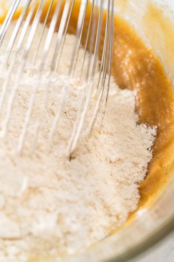 Islak ve kuru malzemelerle karıştırılmış cam bir kabın içinde çırpılmış beyaz çikolatalı makadamia fındığı..