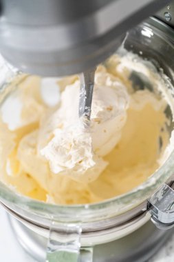 Whisking buttercream frosting in a glass mixing bowl with an electric kitchen mixer for American flag mini cupcakes.