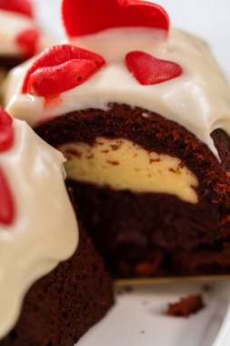 Slicing freshly baked red velvet bundt cake with chocolate lips and hearts over cream cheese glaze for Valentines Day.