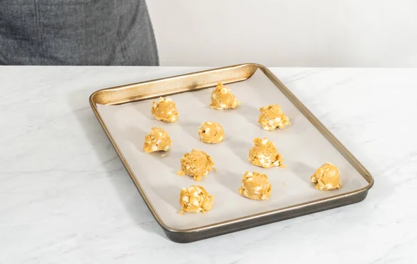 Scooping cookie batter with dough scoop into a baking sheet lined with parchment paper to bake white chocolate macadamia nut.