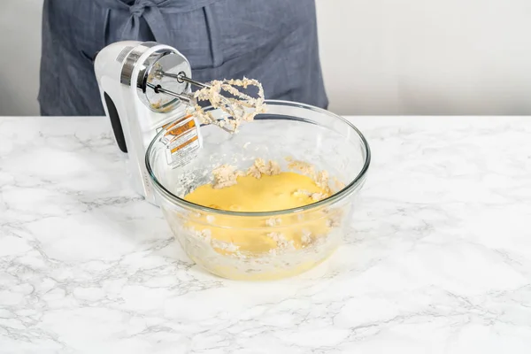 Mixing ingredients with a hand mixer in a large mixing bowl to bake eggnog bundt cake.