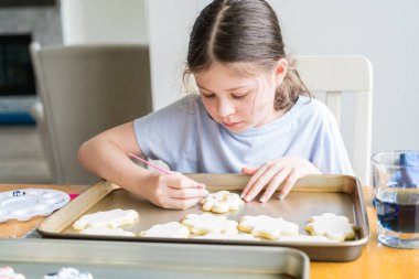 Küçük bir kızın özenle yazdığı iç açıcı bir sahne. Şekerli kurabiyelerin üzerine besin boyası sürmüş. Kurabiyeler güzel bir şekilde beyaz kraliyet kreması ile dolmuş..
