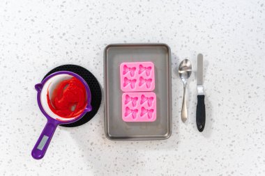 Flat lay. Filling bow silicone chocolate mold with melted chocolate to make a chocolate pretzel Christmas wreath.