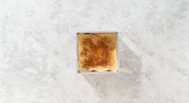 Düz yatıyordu. Kare bir peynirli kek pişirme tavasında parşömen kağıdıyla kaplanmış taze yapılmış ev yapımı yumurta likörü..