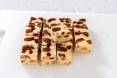 Beyaz çikolatalı fındıklı fındıklı şekerlemeyi beyaz bir kesme tahtasında küçük parçalara ayırmak..