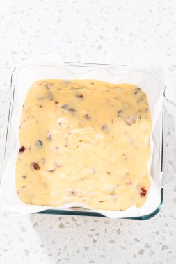 Beyaz çikolatalı fındıklı fındıklı çikolatalı şekerlemeyi hazırlamak için parşömen kağıdıyla kaplanmış fırın tavasına şekerleme döküyorum..