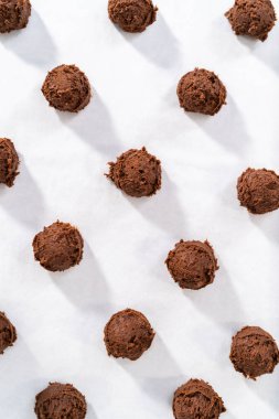 Scooping cookie dough with dough scoop into a baking sheet lined with parchment paper to bake chocolate cookies with chocolate hearts for Valentines Day.