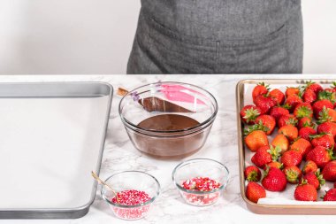 Çikolata kaplı çilekleri hazırlamak için erimiş çikolataya çilek bandırıyorum..