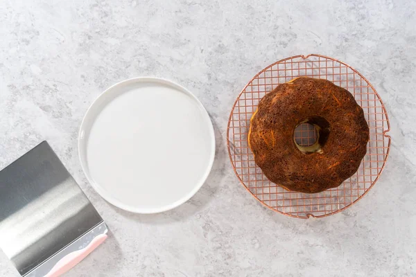 Flat lay. Transferring cooled freshly baked carrot bundt cake from the round cooling rack to the serving plate.