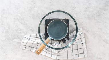 Düz yatıyordu. Eriyen beyaz çikolata parçaları ve diğer malzemeler kaynamış suyun üzerine karıştırıp çubuk şekerleme hazırlıyor..