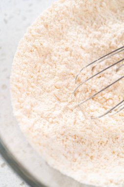 Basit bir vanilyalı kek pişirmek için büyük bir bardakta çırpma kabıyla kuru malzemeyi karıştırıyorum..