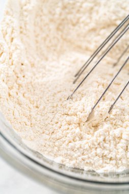 Beyaz çikolatalı macadamia fındığı pişirmek için bardakta çırpma kabıyla kurutulmuş malzemeleri karıştırıyorum..