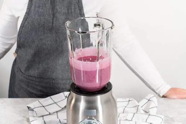 Mixing ingredients in kitchen blender to prepare mixed berry boba smoothie.