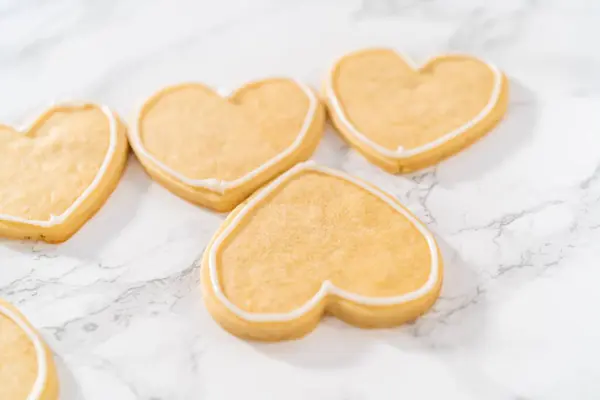 Decorating heart-shaped sugar cookies with pink and white royal icing for Valentines Day.