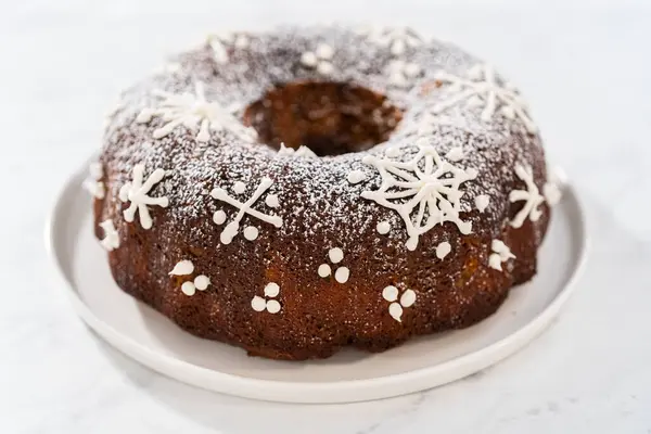Gingerbread bundt cake with caramel filling, buttercream frosting, and powdered sugar dusting on the kitchen counter.