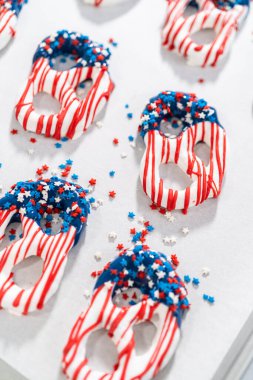 Dipping pretzels twists into melted chocolate to make red, white, and blue chocolate-covered pretzel twists.