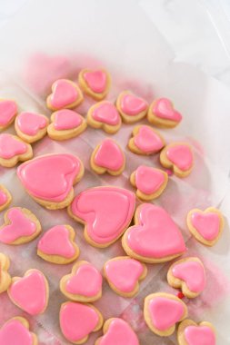 Kalp şeklinde şeker kurabiyelerini büyük plastik bir kapta pembe ve beyaz kraliyet kreması ile depolamak.