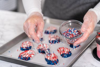 Dipping pretzels twists into melted chocolate to make red, white, and blue chocolate-covered pretzel twists.