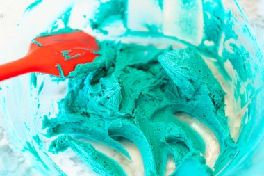 İyi ışıklandırılmış bir mutfakta, yeşil ve diğer renklerin çeşitli tonlarında tereyağlı krema çeşitleri büyüleyici kapkeklerin sanatsal dekorasyonu için titizlikle karıştırılıyor ve hazırlanıyor.