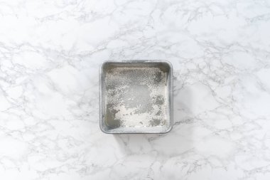 Flat lay. Greasing metal square baking pan to bake sweets.